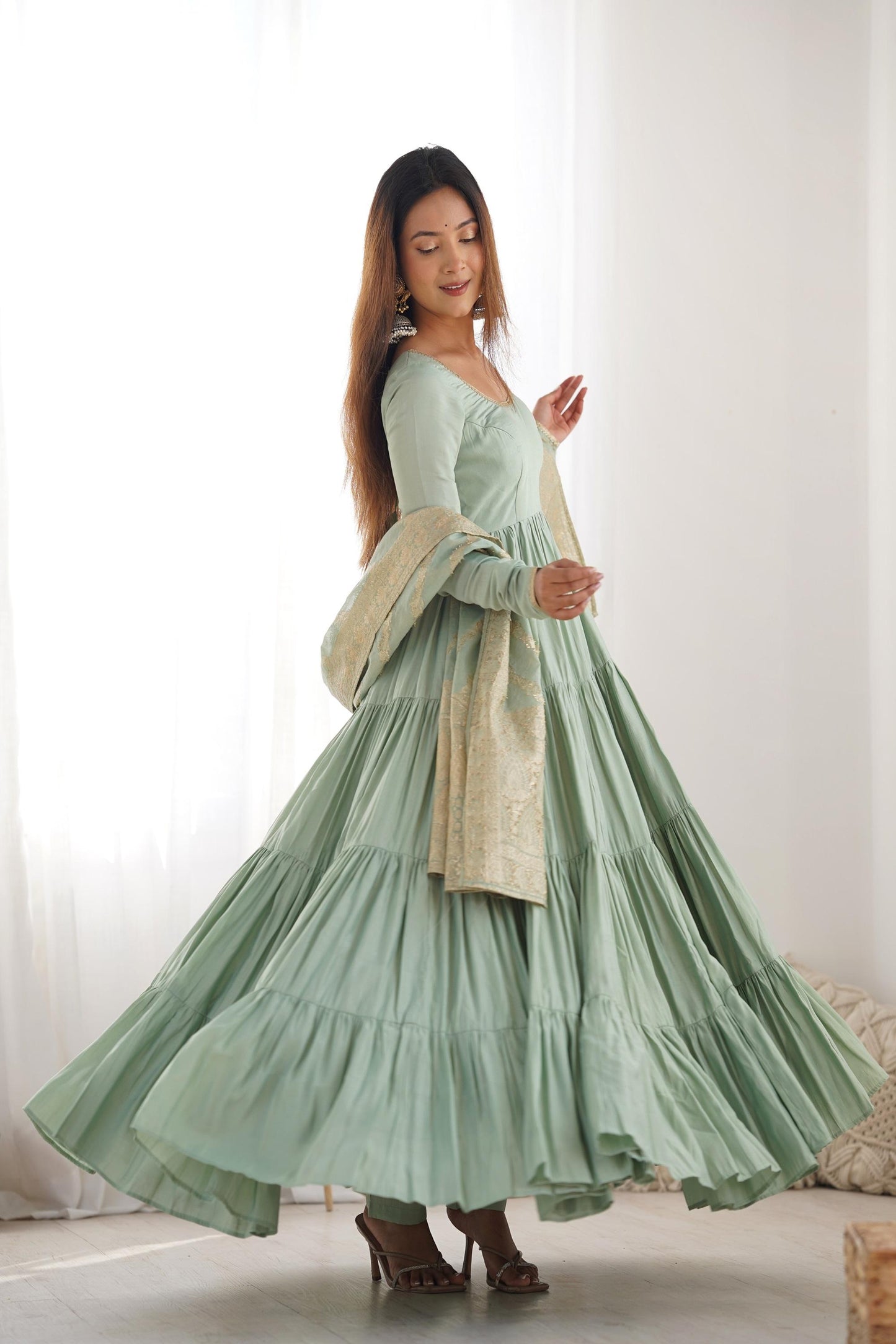 A woman wearing a flowing light green Anarkali suit with a heavy zari woven dupatta